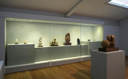 A display case set into the wall holding small sculptures carved from stone, including a head, a woman stretching, and others more abstract in nature.