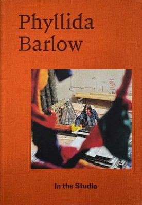 Cover of the book Phyllida Barlow: In the Studio, with a photo of the artist in her studio on an orange cover.