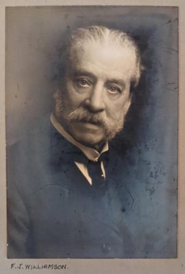 Black and white portrait photo of a formally dressed older man with a mutton chops beard.