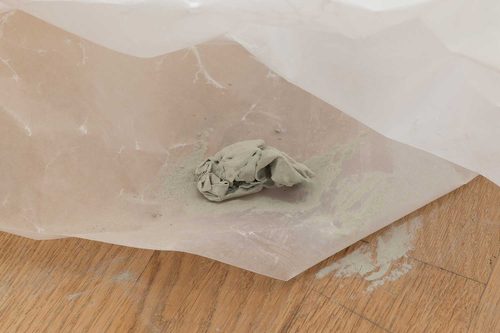Scrunched up material covered in grey dust, sitting on top of a sheet of waxed paper.