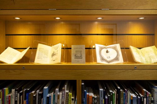 Display cabinet in a library bookcase, showing five books opened to illustrated pages.