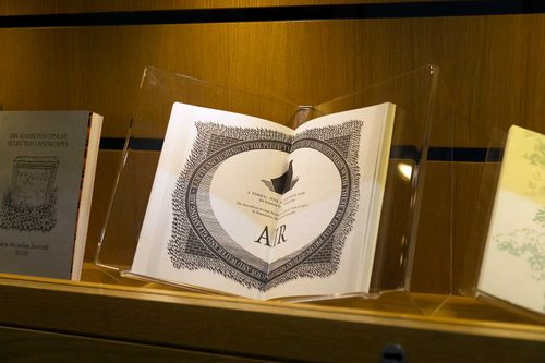 A book in a display case, opened at a page with an illustration of a memorial plaque.